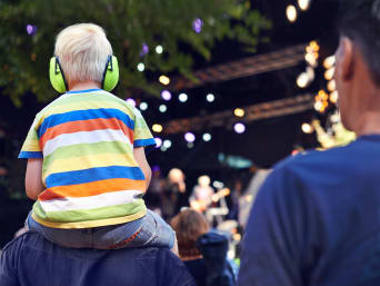 Familienfestivals: Kleiner Junge mit Kindergehörschutz sitzt auf den Schultern seines Vaters.