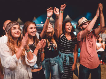 Festivalgoers in stylish festival looks and cheers on a band.