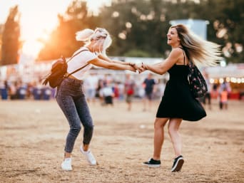 Sporty outfits for festivals: friends dancing together on a field at a festival.