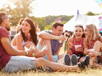 Festiwalowy niezbędnik: przyjaciele siedzący razem przy posiłku na trawniku festiwalowym.