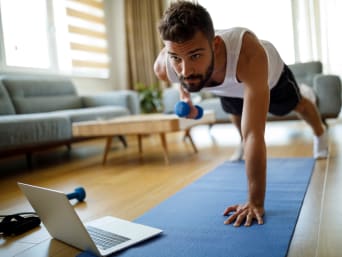 Workout für zuhause – Mann trainiert mit Hanteln zuhause vorm Laptop.