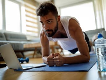 Online Fitnessen: Jonge man doet een plank met behulp van een fitness video.