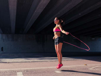 Corde à sauter : une femme sautant avec une corde en caoutchouc rose.