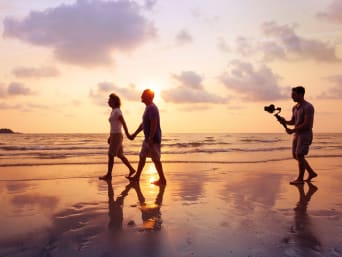 Cómo hacer vídeos: un cineasta aficionado graba en vídeo a una pareja por la playa.
