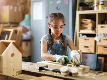 Knutselen voor kinderen: meisje maakt houtwerk in een houtwerkplaats.