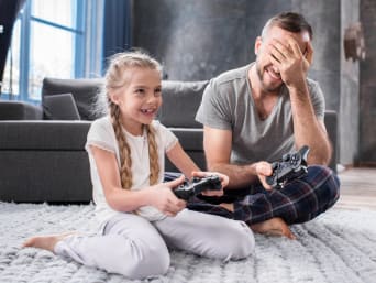 Hoe lang mogen kinderen gamen? Vader helpt dochter bij het gamen.