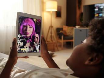 Welche Risiken birgt Twitch für Kinder? – Teenager schaut einen Livestream auf dem Tablet. Welche Risiken birgt Twitch für Kinder? – Teenager schaut einen Livestream auf dem Tablet.