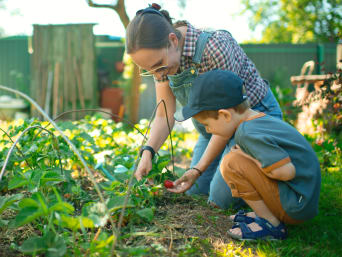 Tuinieren met kinderen: een moeder toont haar zoon een aardbeiplant in de tuin.