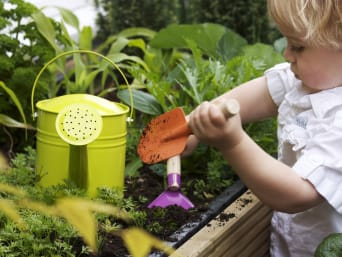 Narzędzia dla dzieci do ogrodu: maluch dba o podwyższone grządki.