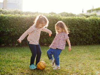 Jak urządzić ogródek dla dzieci – rodzeństwo gra w piłkę w ogrodzie.