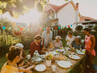 Vyrobte si svou vlastní dekoraci na zahradní párty: Rodina na zahradě spolu hoduje kolem stolu.