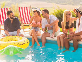 Pool-Party-Outfits: Freunde sitzen in sommerlichen Outfits am Pool.