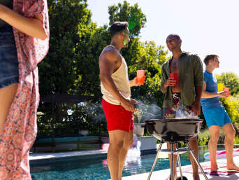 Ideen für Pool-Party-Outfits: Männer stehen am Pool und Grillen.