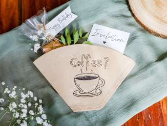 Geschenkideen für Mama: Selbstgemachte Einladung zum Kaffee liegt auf einem Tisch. Geschenkideen für Mama: Selbstgemachte Einladung zum Kaffee liegt auf einem Tisch.