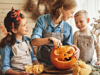 Kürbis schnitzen: Eine Mutter höhlt mit ihren Kindern einen Halloween-Kürbis aus.