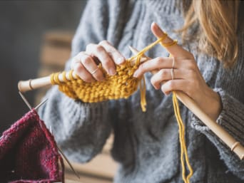 Stricken lernen – Eine Frau strickt mit gelber Wolle.
