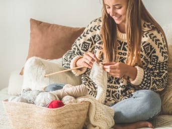 Jak zacząć robić na drutach? Dziewczyna siedzi na łóżku i robi na drutach biały szal.