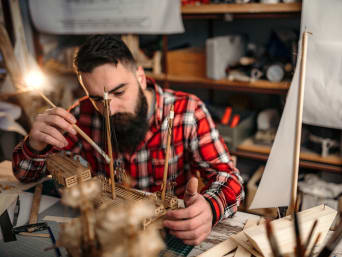 Kreatywne hobby dla dorosłych: mężczyzna składa model statku z drewna. 