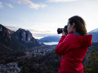 Photographie de paysage : une femme fait une photo de montagnes et d’un lac avec son appareil.