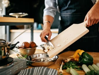 Leren koken - amateurkok doet gesneden ingrediënten in een pan.