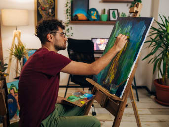 Kreativní koníček: Muž maluje abstraktní obraz na stojanu.