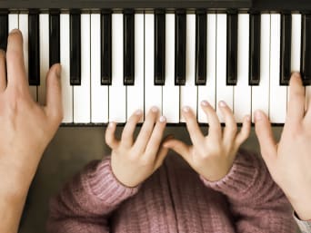 Musikinstrumente Kinder – Eltern spielen gemeinsam mit dem Kind Klavier.