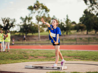 Entrenamiento de atletismo para niños: una niña practica lanzamiento de peso.