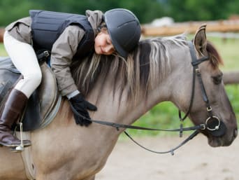 Reitunterricht: Mädchen mit Rückenprotektor und Helm sitzt auf Pferd.
