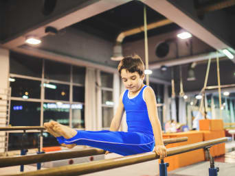 Tipos de gimnasia para niños: un niño hace ejercicios en un aparato de gimnasia.