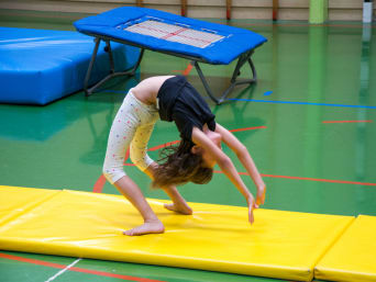 Gimnasia para niños: una niña realiza un remonte hacia atrás en una clase de gimnasia.