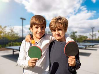 Tischtennis für Kinder: Zwei befreundete Jungs umarmen sich und halten dabei einen Tischtennis-Schläger.