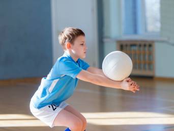 Volleyball Kinder – Junge balanciert einen Volleyball auf seinen Unterarmen.