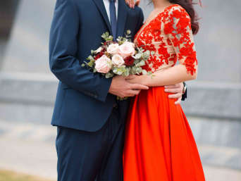 Alternative Hochzeitskleider: Braut im roten Hochzeitskleid und Bräutigam halten gemeinsam den Brautstrauß.
