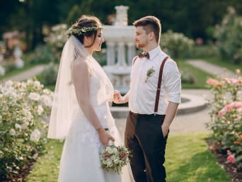 Bruidegompak vintage met bretels – bruidspaar in een tuin met bloemen.