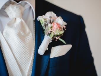 Outfits for a registry office wedding: a groom wearing a patterned tie with a thick tie knot and a flower pin.