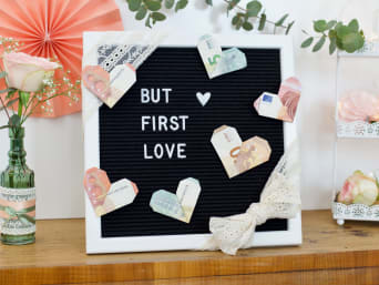 Geldcadeaus bruiloft DIY: geld wordt in hartjesvorm aan een letterbord bevestigd.