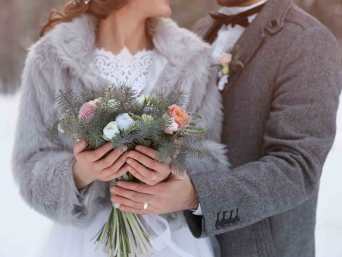 Winterhochzeit-Outfit: Brautpaar im Schnee hält gemeinsam den Brautstrauß. Winterhochzeit-Outfit: Brautpaar im Schnee hält gemeinsam den Brautstrauß.