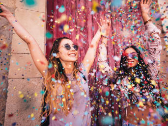 Hippies kostým: dvě ženy rozhazují barevné konfety během karnevalového průvodu.