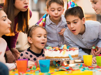 Organizar un cumpleaños infantil: una niña sopla la vela de la tarta de cumpleaños.