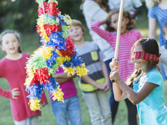 Juegos para fiestas de cumpleaños: una niña con los ojos tapados delante de una piñata.
