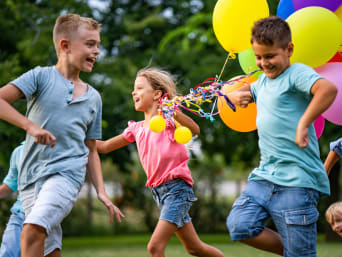 Juegos para una fiesta infantil de cumpleaños: niños corriendo con globos por un jardín.