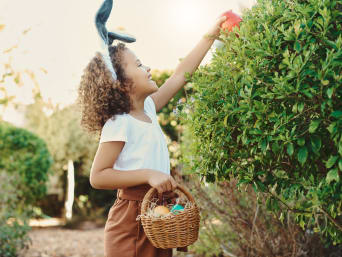 Velikonoční dárky pro děti: Dívka hledá velikonoční vajíčka a dárky na zahradě.