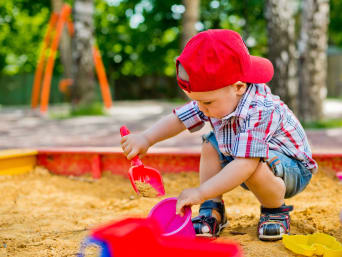 Petits cadeaux de Pâques : un bébé de 2 ans joue avec une pelle et un seau dans un bac à sable.