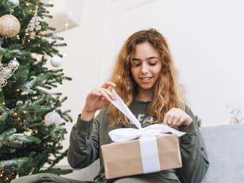 Christmas presents for teenagers – a teenage girl unwrapping her Christmas present.