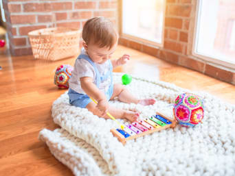Geschenk für 2-Jährige: Kleinkind sitzt auf dem Boden und spielt auf einem Xylophon.