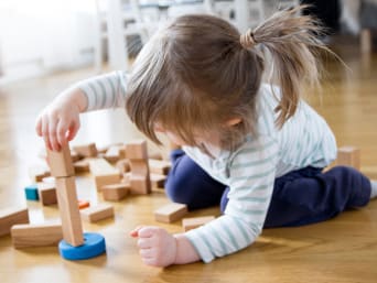 Dárek pro batole: holčička staví věž z dřevěných kostek.