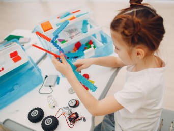 Alt: Gift for 8-year-olds: a little girl assembles a robot with a kit.