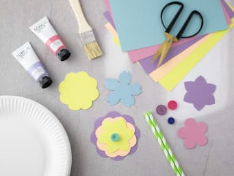 Bloemen knutselen: gekleurd knutselpapier, papieren bordje en andere knutselmaterialen liggen op een tafel.