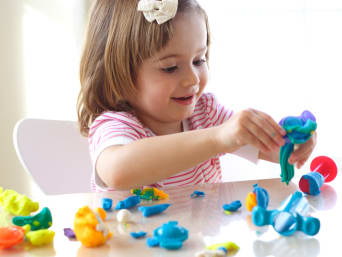 Cadeaus voor kinderdag: kleuter bewerkt kleurrijke boetseerklei op tafel.