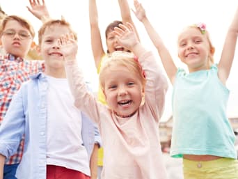 Festa dei bambini: un gruppo di bambini sorride e alza le braccia al cielo.